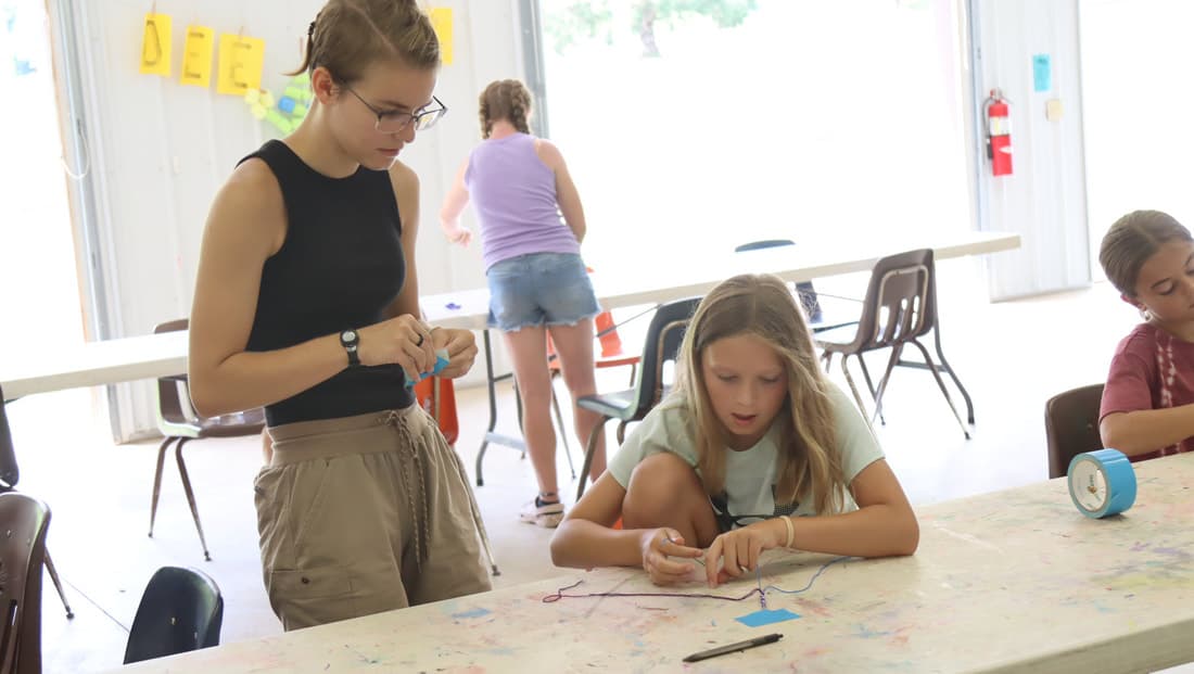 Craft leader helping campers with projects at Camp Otyokwah